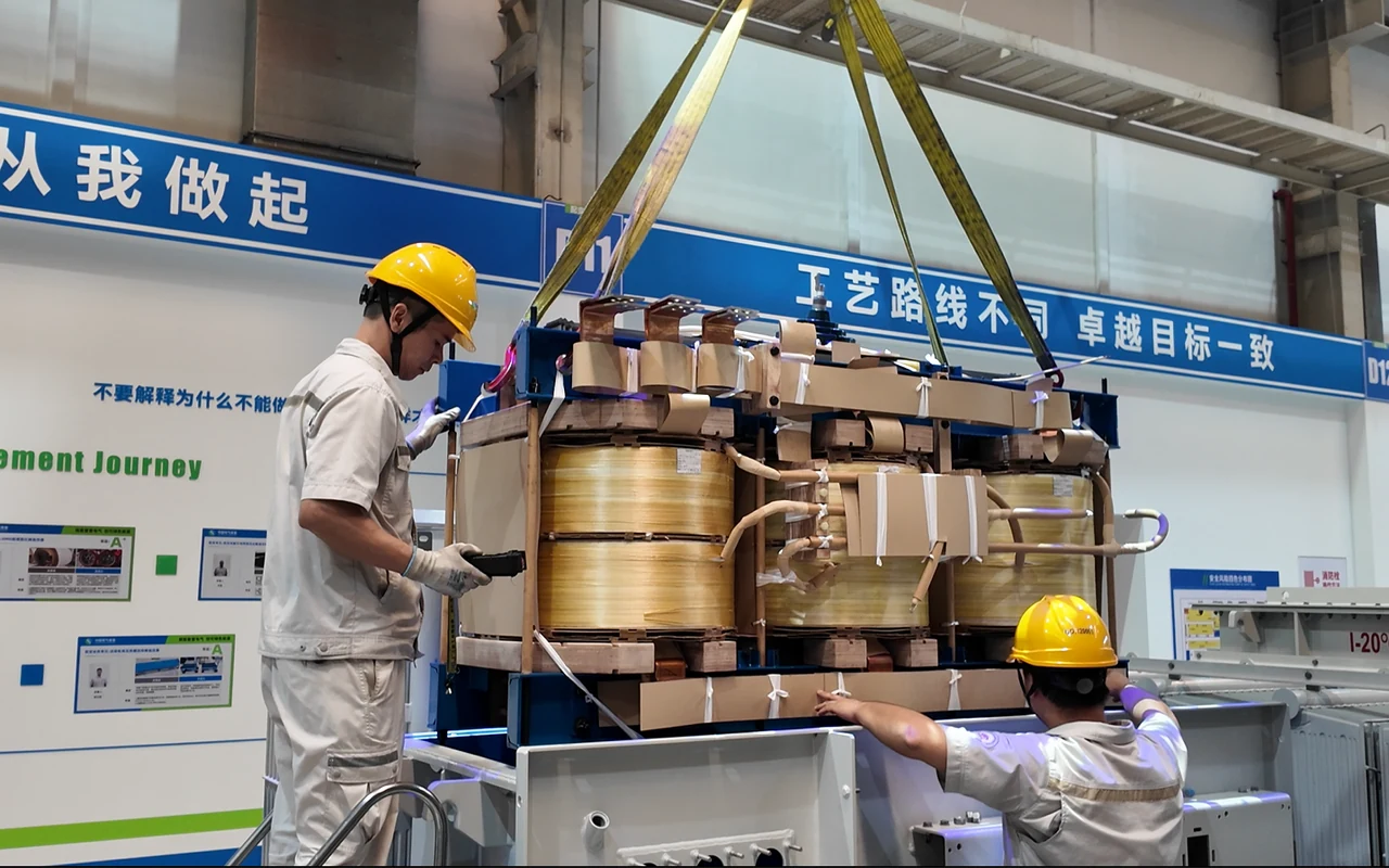 Workers lowering the transformer active part into its tank during final assembly